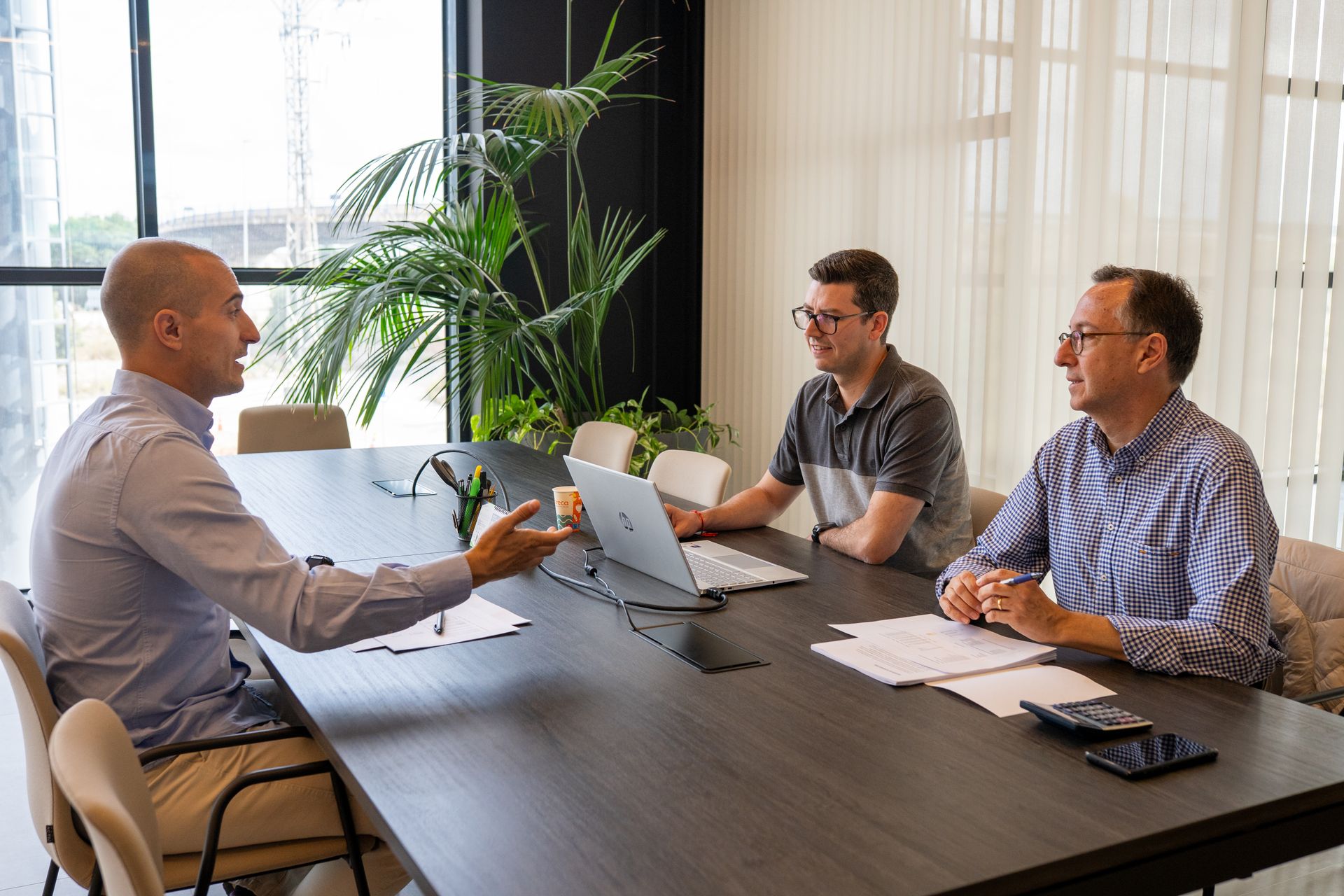 Three professionals discussing employment status and IR35 at an office meeting table, with a laptop, documents and a calculator in front of them.